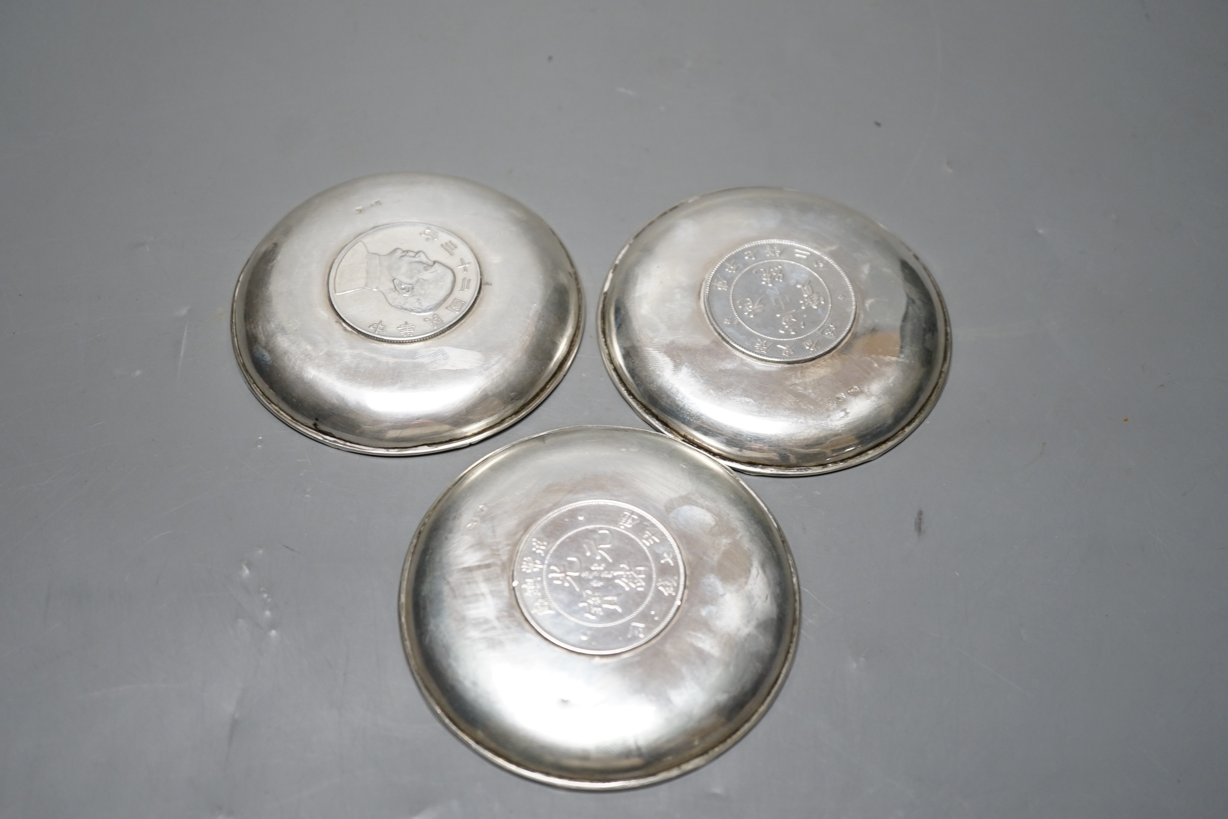 Three Chinese white metal dishes, each inset with coin, maker HC, 94mm, 196 grams gross.